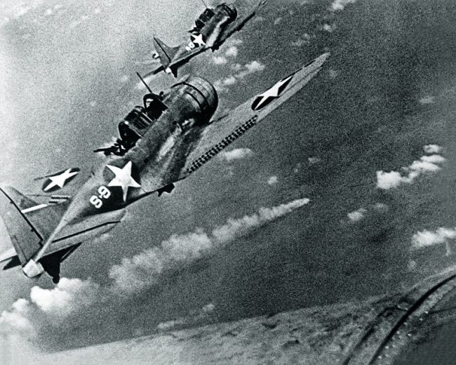 U.S. Navy Douglas SBD-3 'Dauntless' dive bombers from scouting squadron VS-8 from the aircraft carrier USS Hornet (CV-8) approaching the burning Japanese heavy cruiser Mikuma to make the third set of attacks on her, during the Battle of Midway, 6 June 1942.
