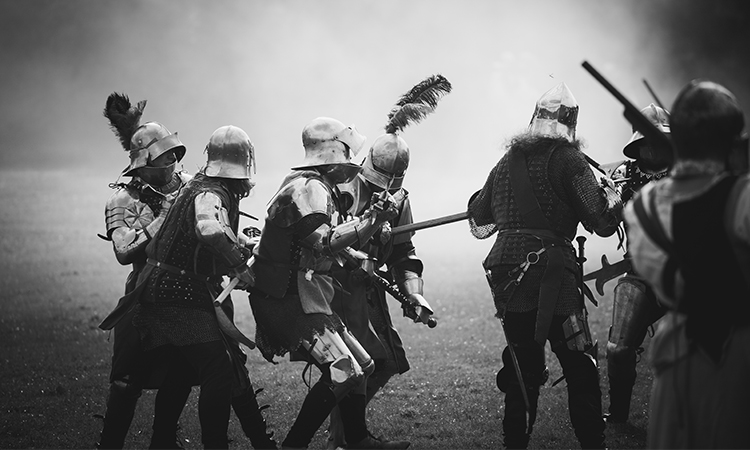 Several re-enactors in armour fight in a misty scene